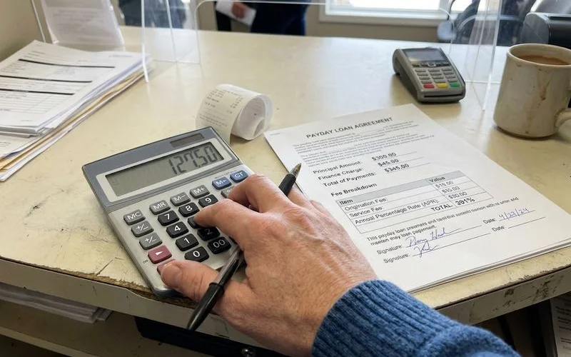 A calculator, cash, and a loan agreement on a counter representing the true cost of a short-term loan