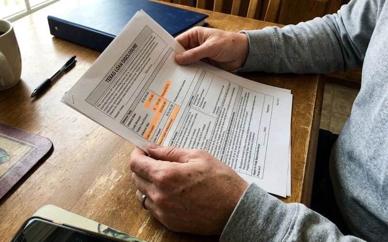 A borrower reviewing a loan disclosure form at a storefront lender's counter before signing